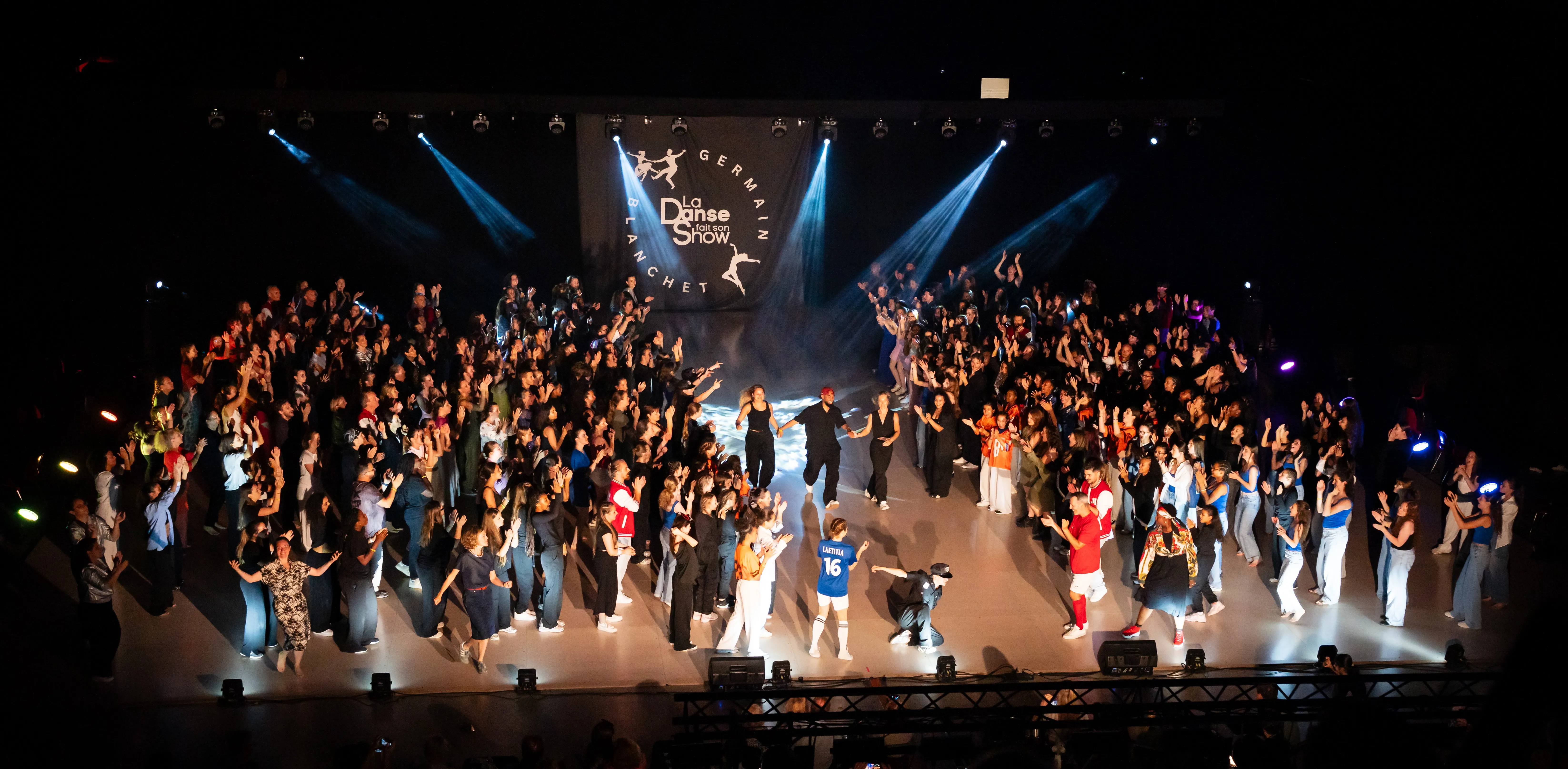 Plateau de danseurs saluant sur scène sous les projecteurs, à la fin d'un spectacle